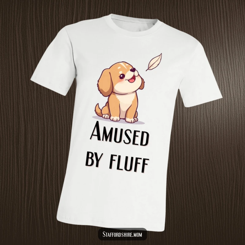 Funny t-shirt showing a solid build dog looking up with wide-eyed amusement at a delicate floating feather.