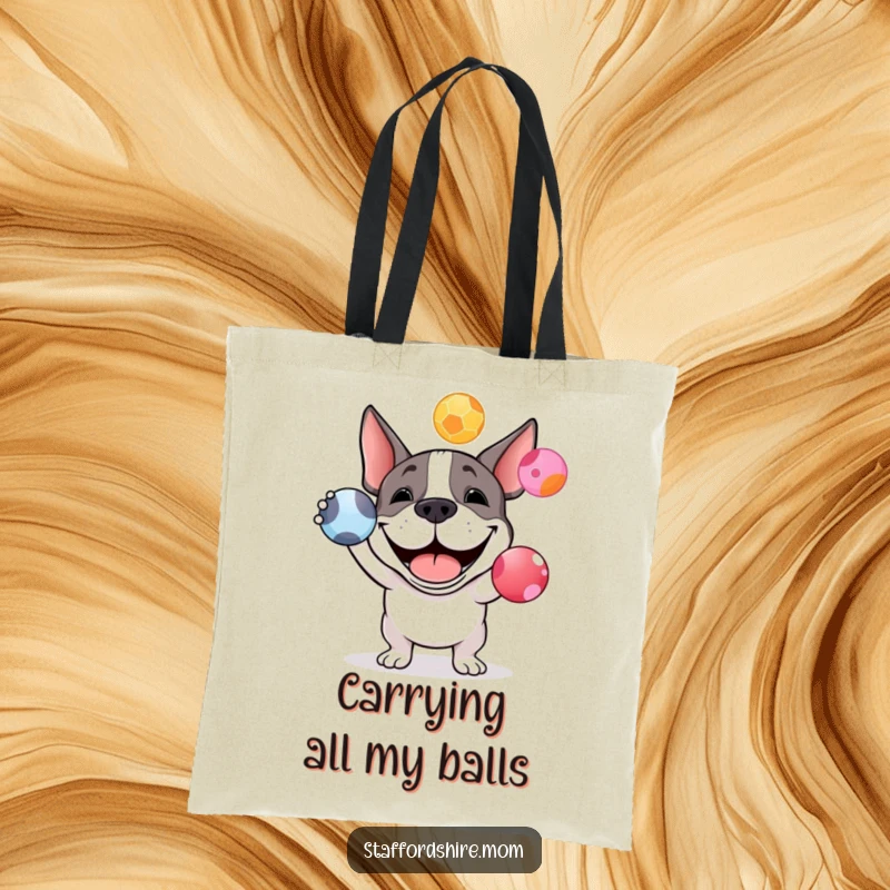 Funny Staffy bull terrier tote bag with a grinning dog attempting to juggle three colorful balls, ideal for carrying items.